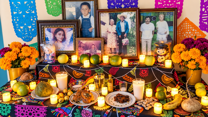 Ofrenda de Día de Muertos en casa con fotos de la familia, cempasúchil, papel picado, velas y pan de muerto